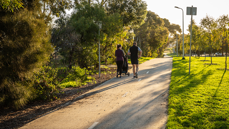 Two people walking on a concrete path surrounded by trees