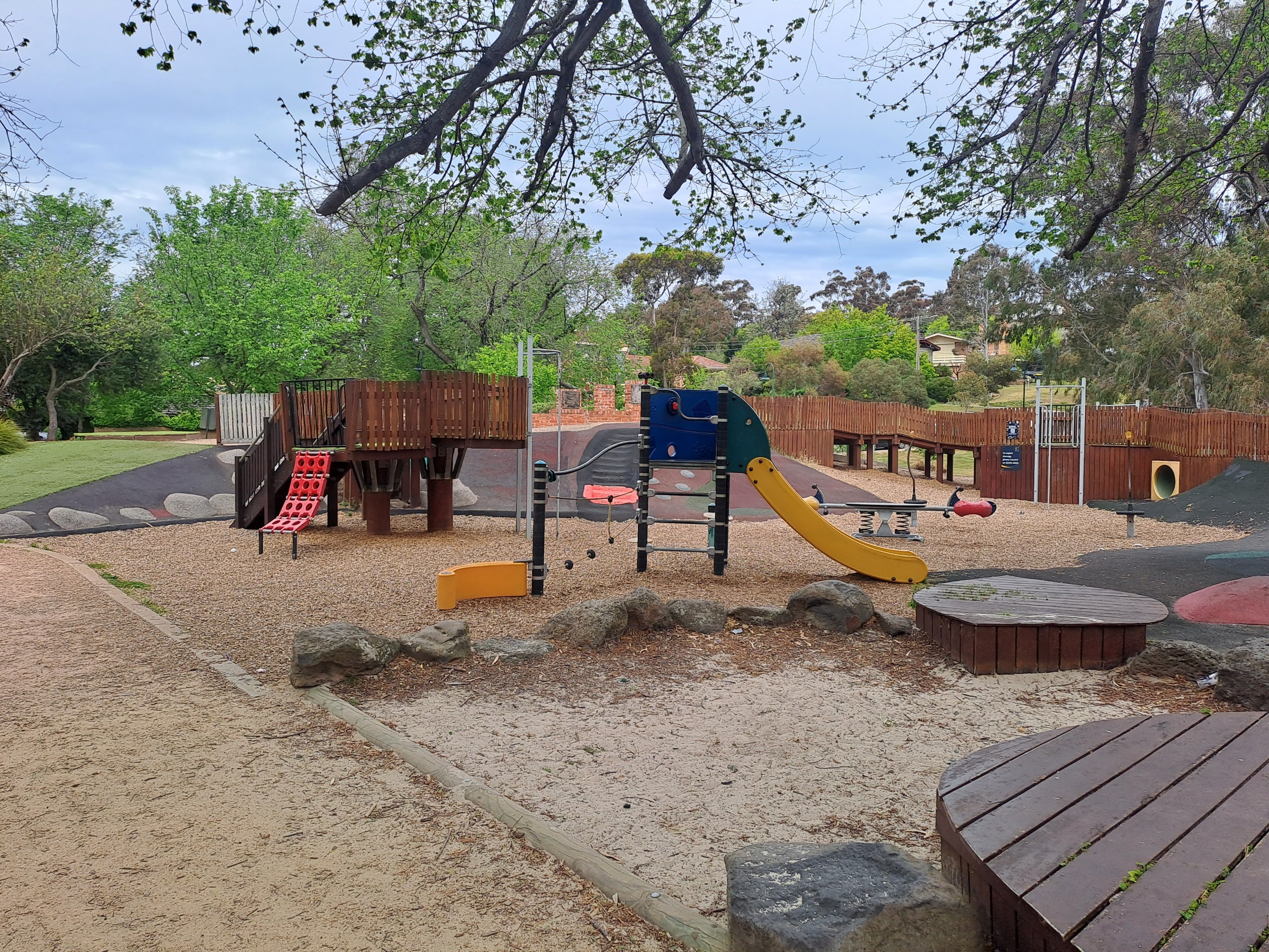 Before: A photo of the playground with a wood play fort and wooden walkway bridge in the background